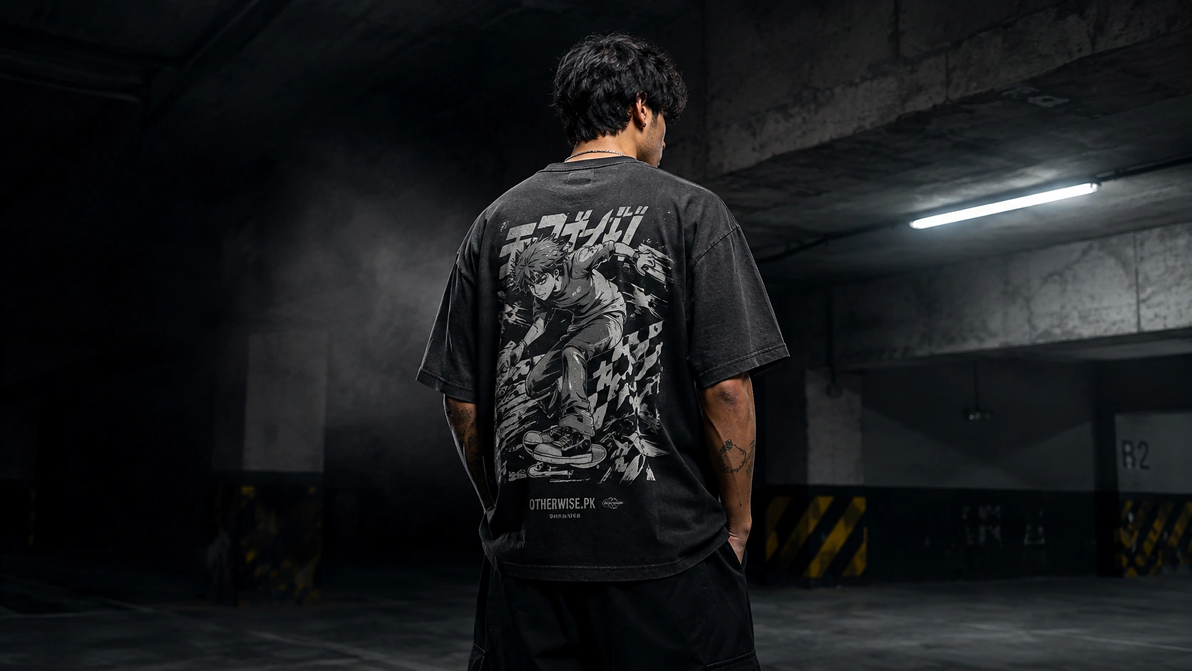 Back view of a young man wearing a black Otherwise.pk graphic T-shirt in a parking garage