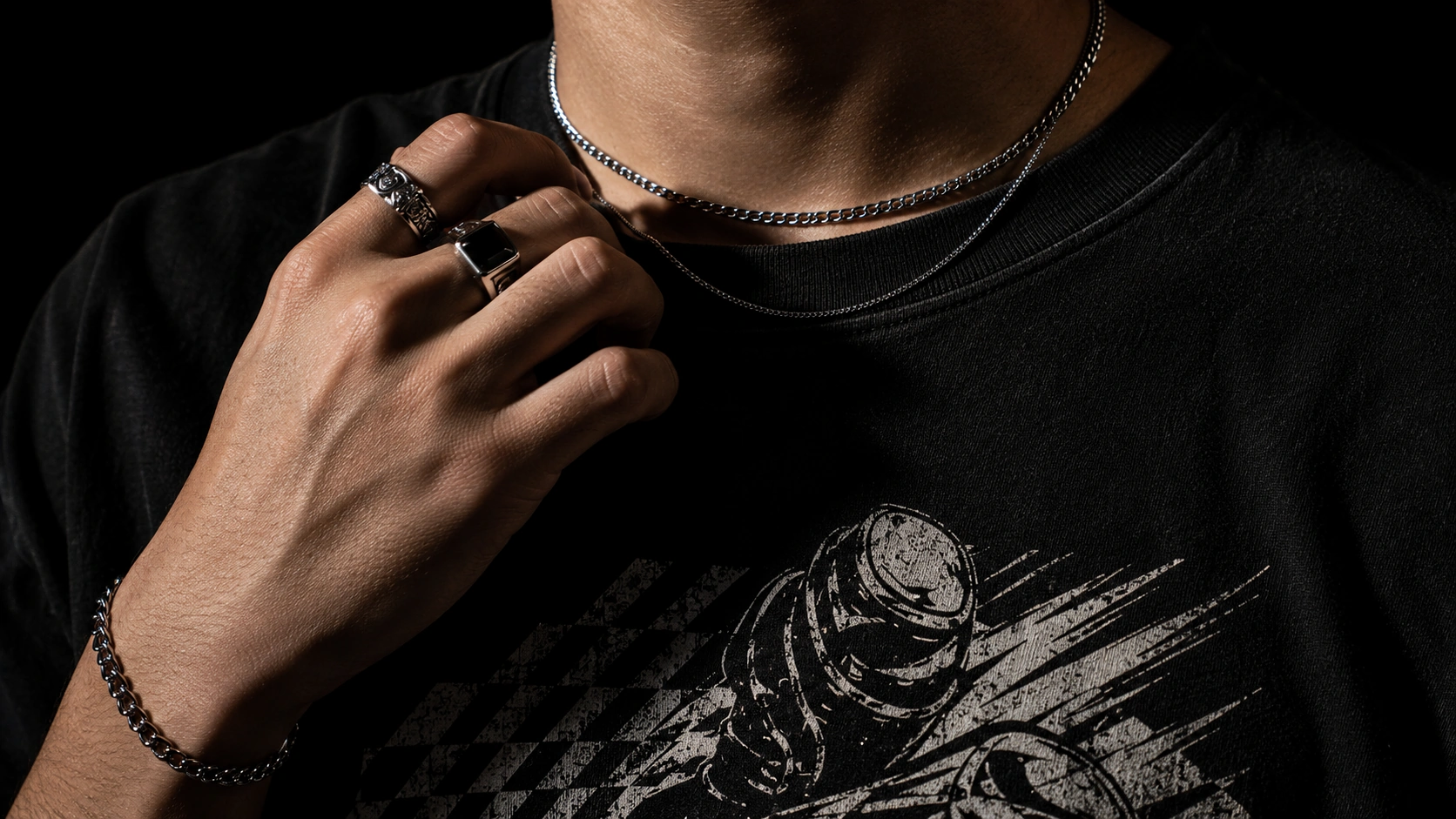 Close-up of a black graphic T-shirt worn with a silver chain necklace and rings
