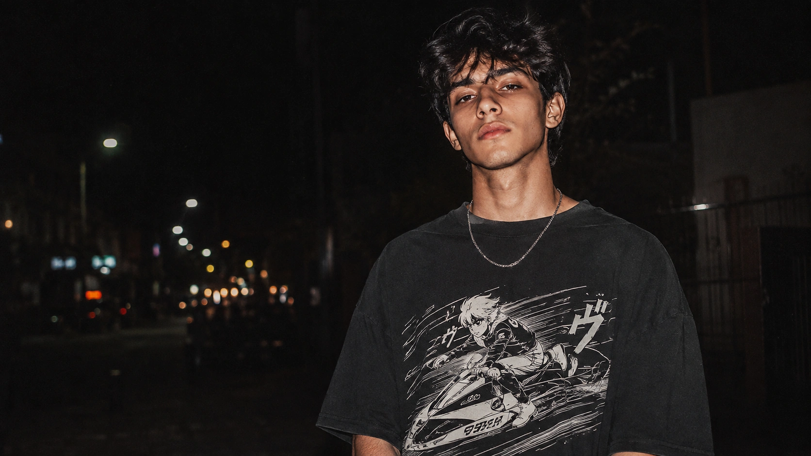 Young man in a black graphic T-shirt on a city street at night